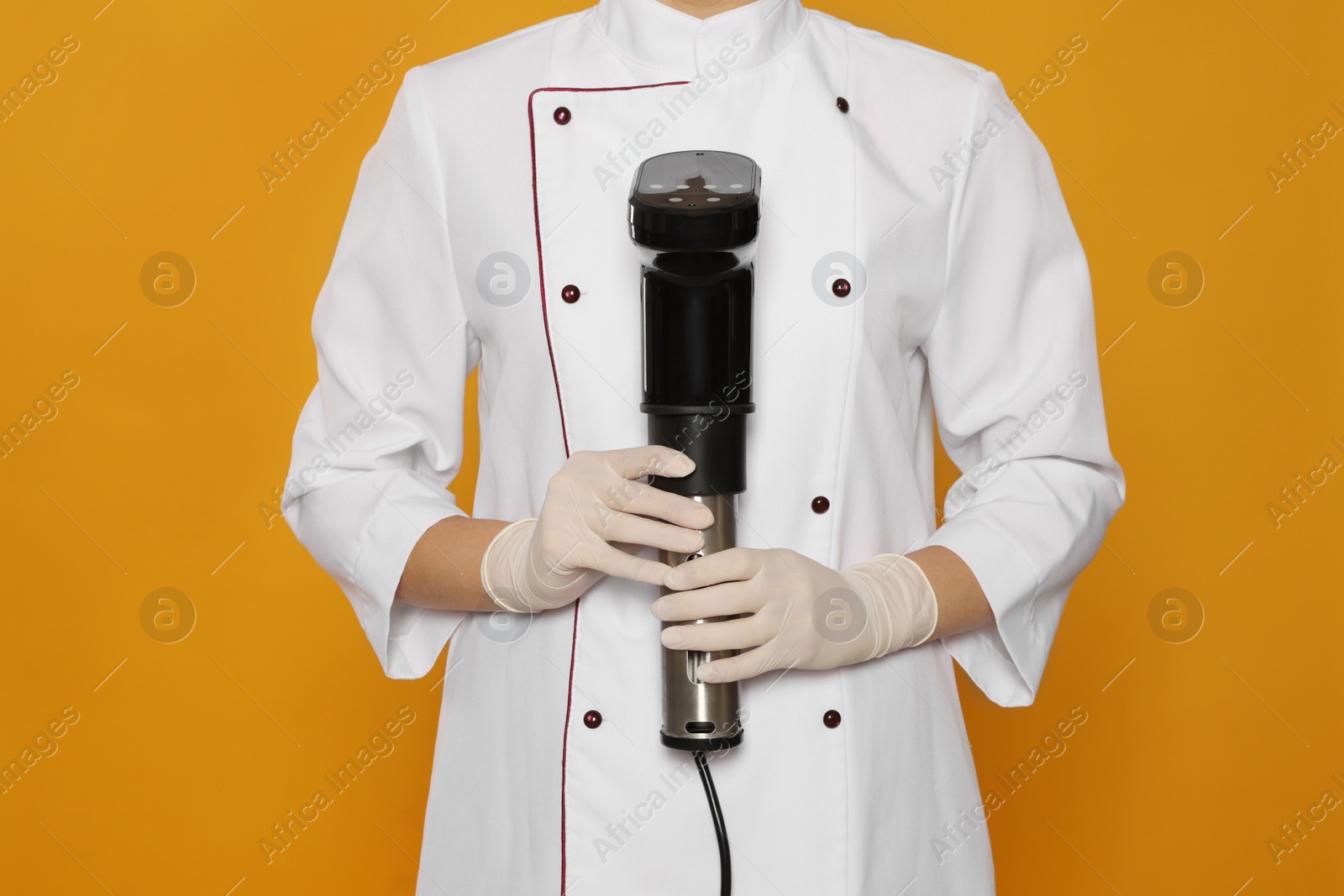Photo of Chef holding sous vide cooker on orange background, closeup