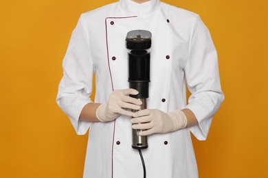Chef holding sous vide cooker on orange background, closeup