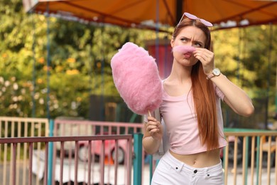 Photo of Beautiful woman having fun with cotton candy at funfair. Space for text