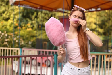 Beautiful woman having fun with cotton candy at funfair. Space for text