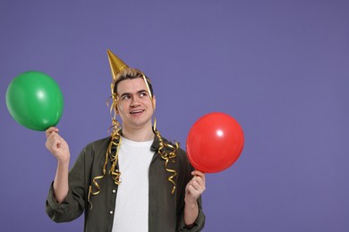 Young man with party hat and balloons on purple background, space for text