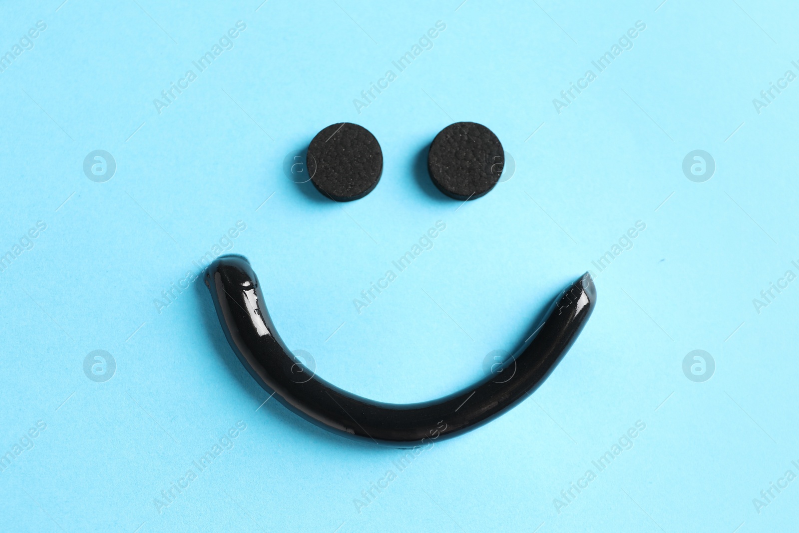 Photo of Smile made from charcoal toothpaste and tablets on light blue background, flat lay