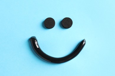 Photo of Smile made from charcoal toothpaste and tablets on light blue background, flat lay