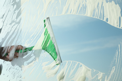 Photo of Woman cleaning window with squeegee on spring day, closeup