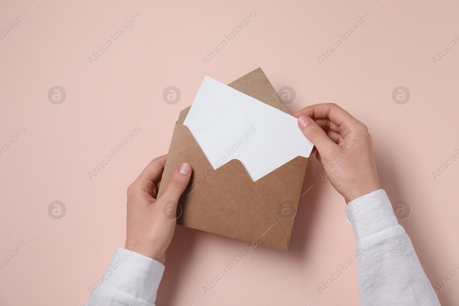 Photo of Woman taking card out of letter envelope at beige table, top view