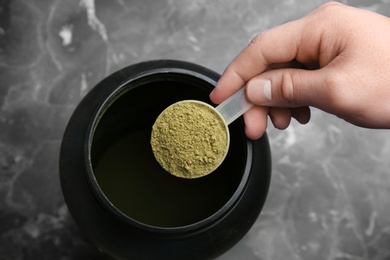 Photo of Man holding measuring spoon with hemp protein powder over jar on table