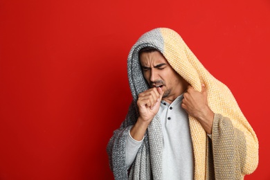 Man wrapped in warm blanket coughing on red background, space for text. Cold symptoms