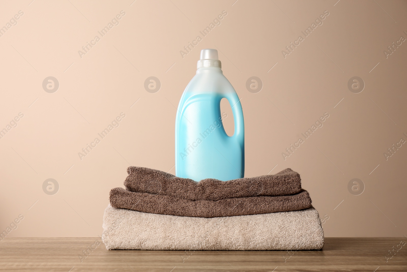 Photo of Bottle of detergent and clean towels on table against color background. Laundry day