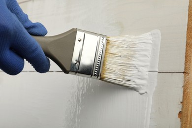 Photo of Worker applying white paint onto wooden surface, closeup