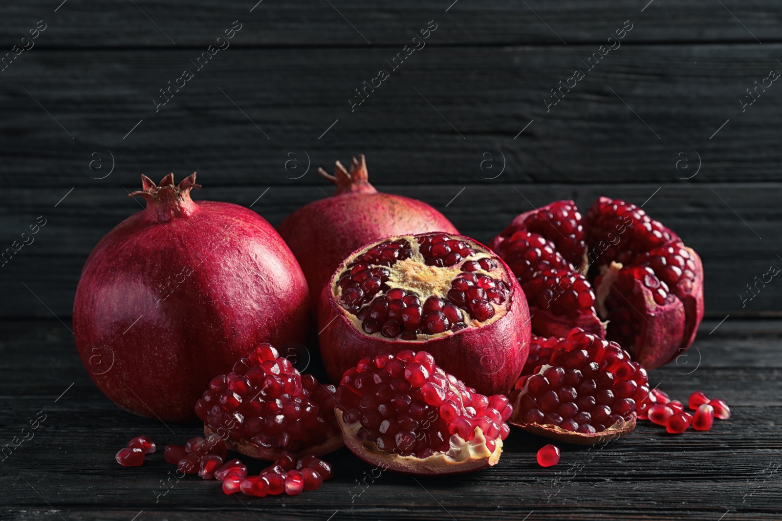 Photo of Ripe pomegranates and seeds on wooden table