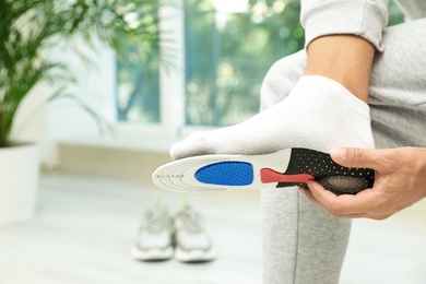Photo of Man fitting orthopedic insole indoors, closeup. Foot care