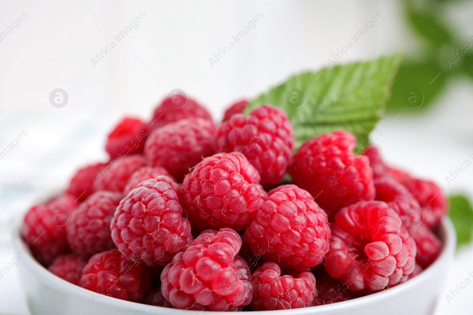 Photo of Fresh ripe raspberries with green leaf in bowl, closeup