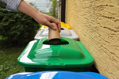 Woman throwing paper coffee cup into recycling bin outdoors, closeup