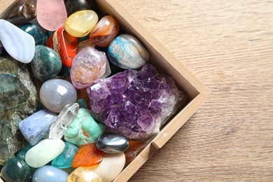 Box with different beautiful gemstones on wooden table, flat lay