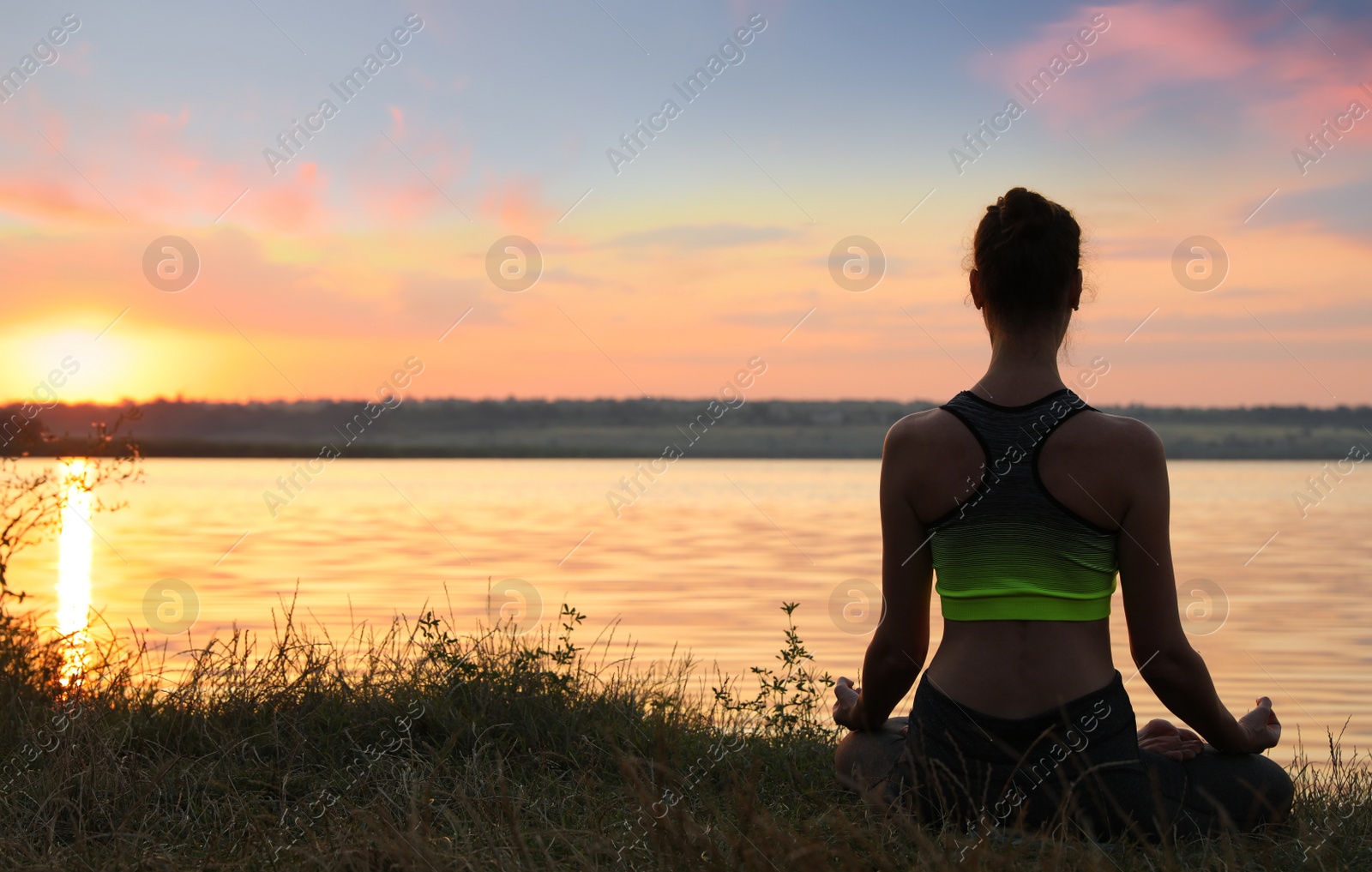 Photo of Woman meditating near river at sunset, back view. Space for text