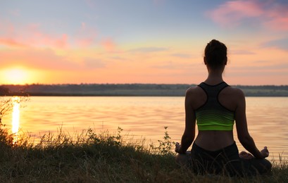 Photo of Woman meditating near river at sunset, back view. Space for text