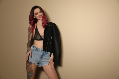 Photo of Beautiful woman with tattoos on body against beige background. Space for text