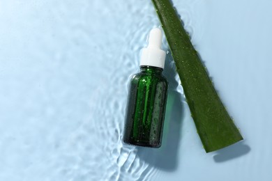 Bottle of cosmetic product and aloe leaf in water on light blue background, flat lay. Space for text