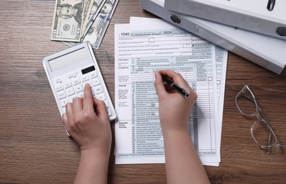 Photo of Payroll. Woman using calculator while working with tax return forms at wooden table, top view