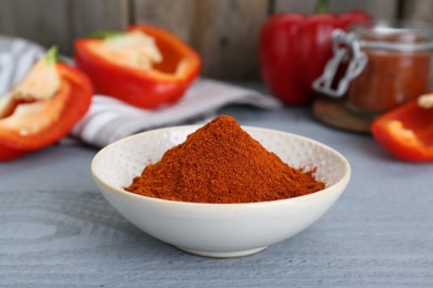 Photo of Bowl with aromatic paprika powder and fresh bell peppers on grey wooden table