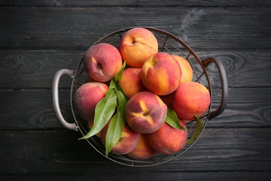 Photo of Fresh sweet peaches in metal basket on black wooden table, top view
