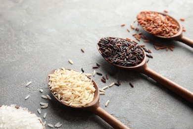 Spoons with different types of rice on grey background. Space for text