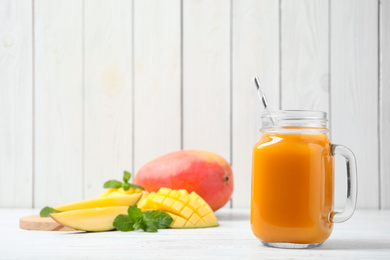 Photo of Fresh delicious mango drink on white wooden table. Space for text