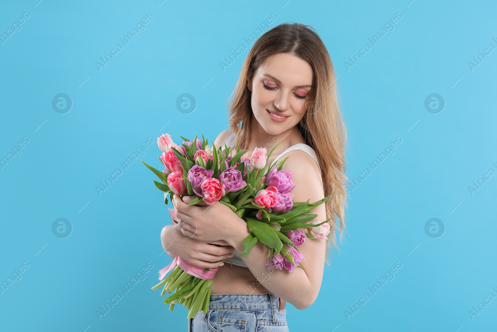 Photo of Happy young woman with bouquet of beautiful tulips on light blue background