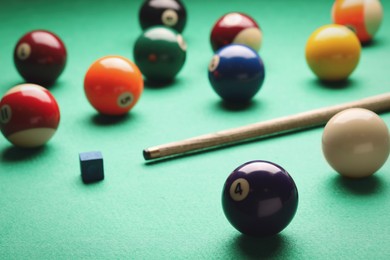 Photo of Many colorful billiard balls, cue and chalk on green table