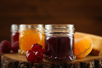 Jars with different sweet jams and ingredients on wooden stump