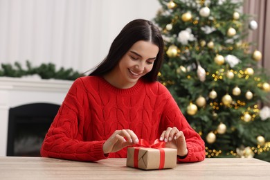 Happy woman opening Christmas gift at wooden table in room