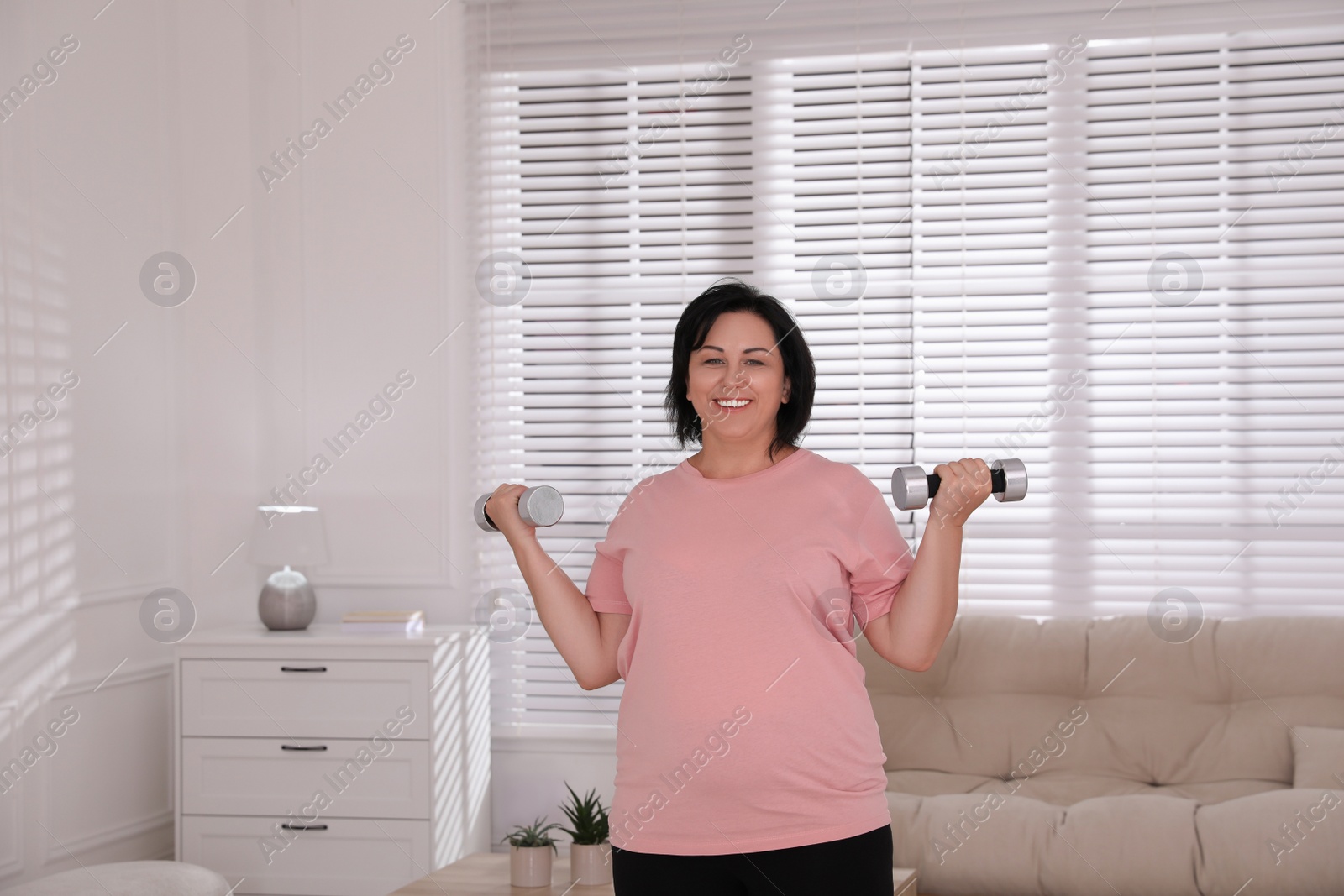 Photo of Overweight mature woman doing exercise with dumbbells at home