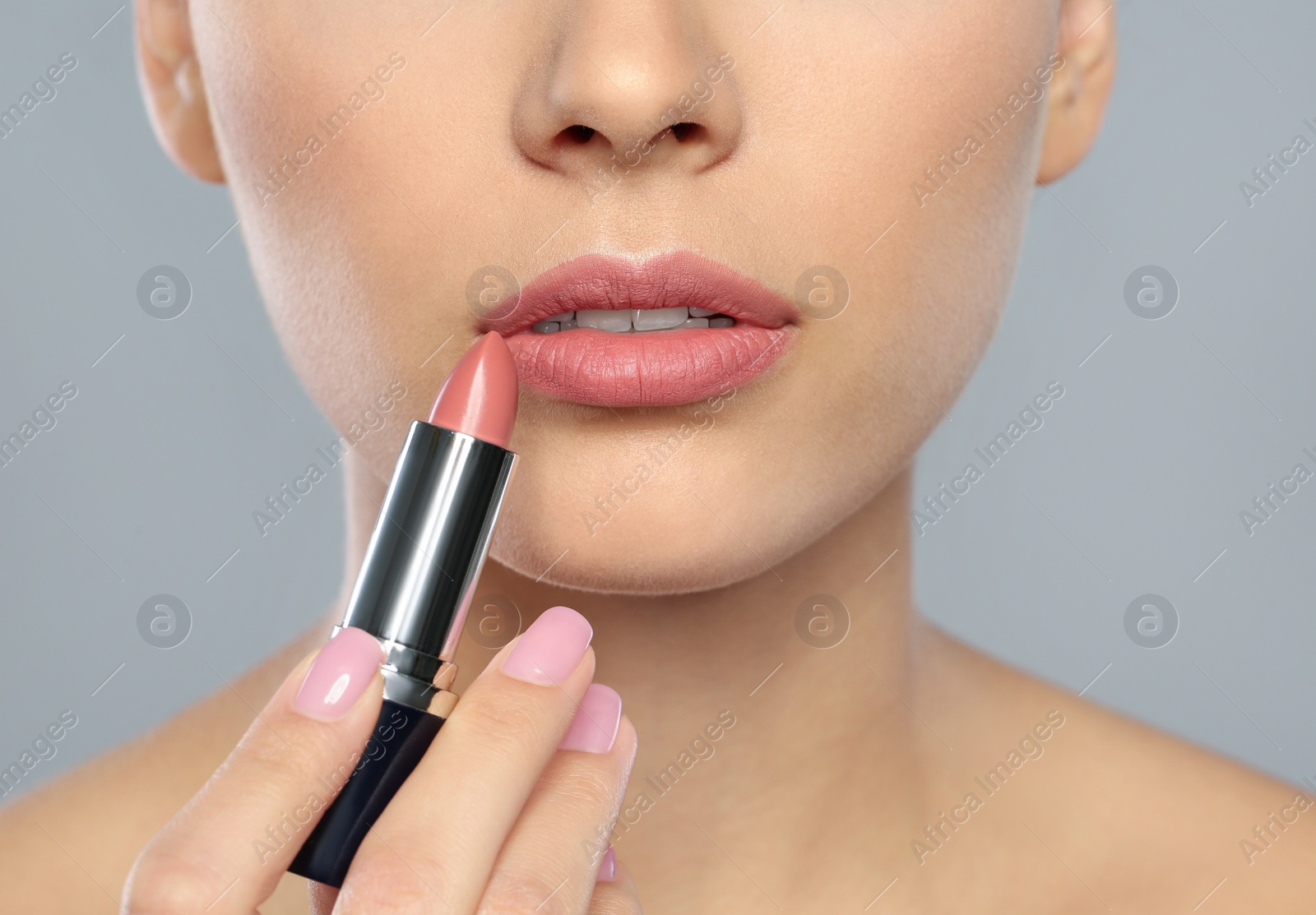 Photo of Young woman applying lipstick on color background, closeup