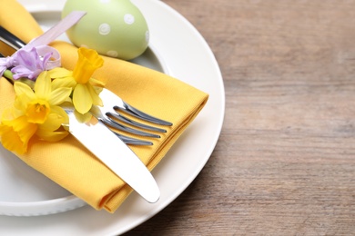 Festive Easter table setting with painted egg and flowers on wooden background, closeup. Space for text