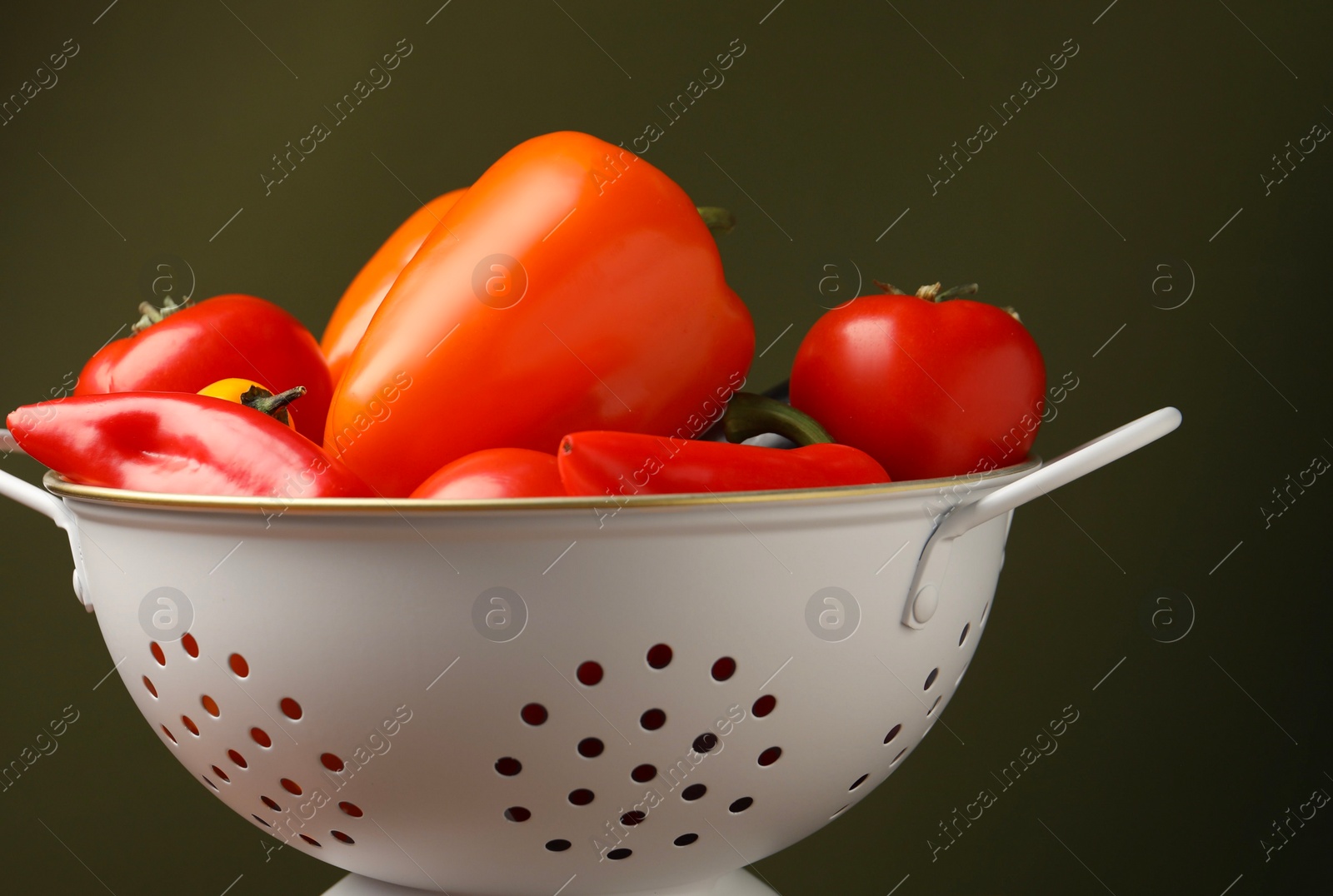 Photo of Colander with fresh vegetables on olive background, closeup