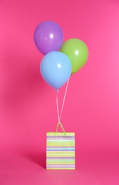 Paper bag with bright air balloons on color background