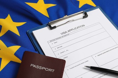 Photo of Visa application form, passport and pen on flag of European Union, closeup