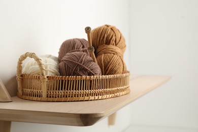 Photo of Woolen yarns and knitting needles in basket on wooden shelf. Space for text
