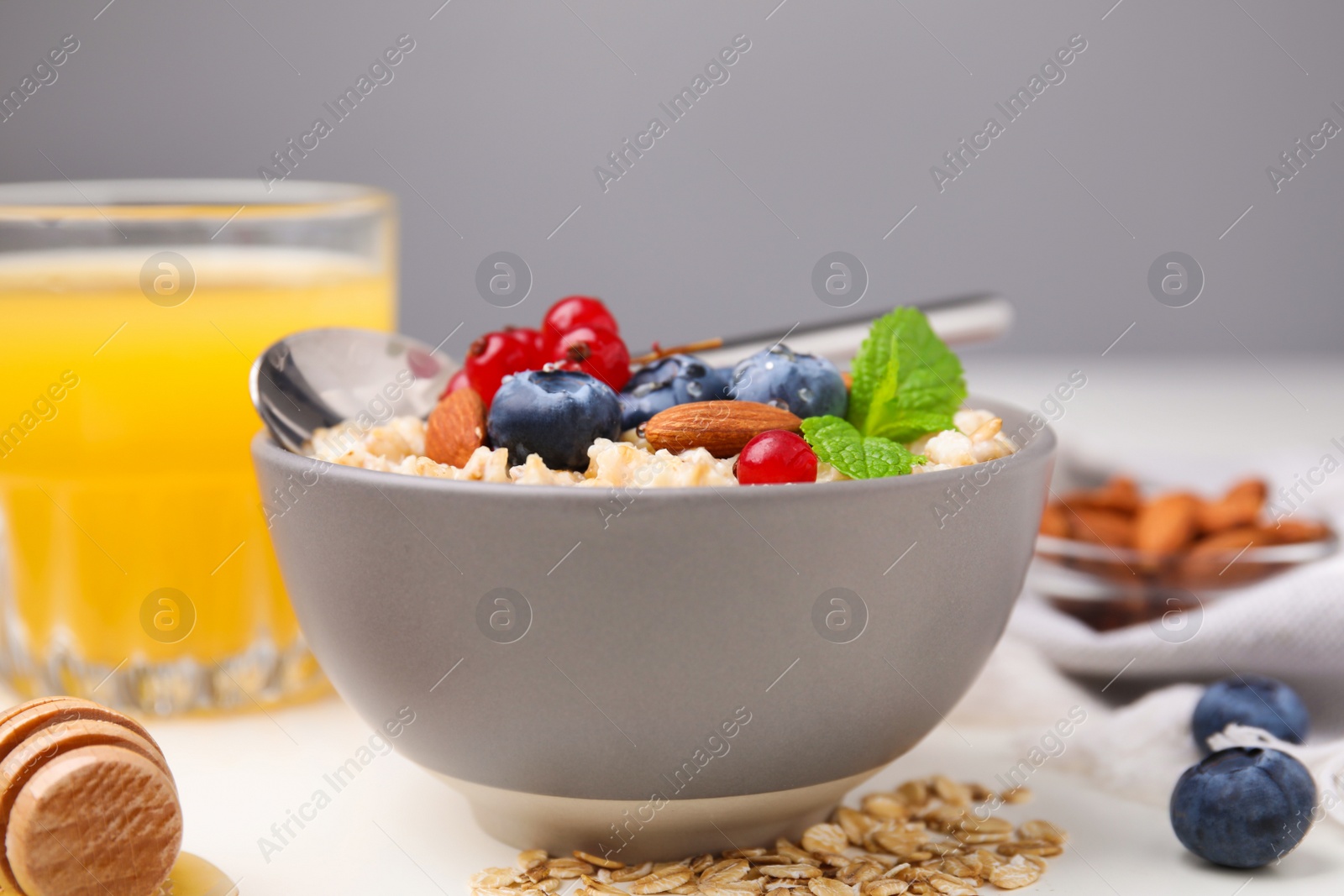 Photo of Oatmeal served with berries, almonds and mint on white table, closeup