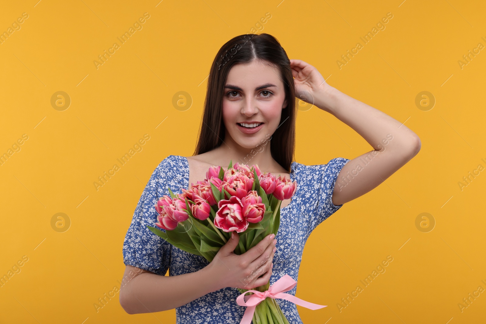 Photo of Happy young woman with beautiful bouquet on orange background