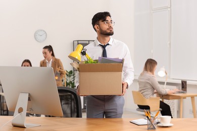 Photo of Unemployment problem. Frustrated man with box of personal belongings at table in office