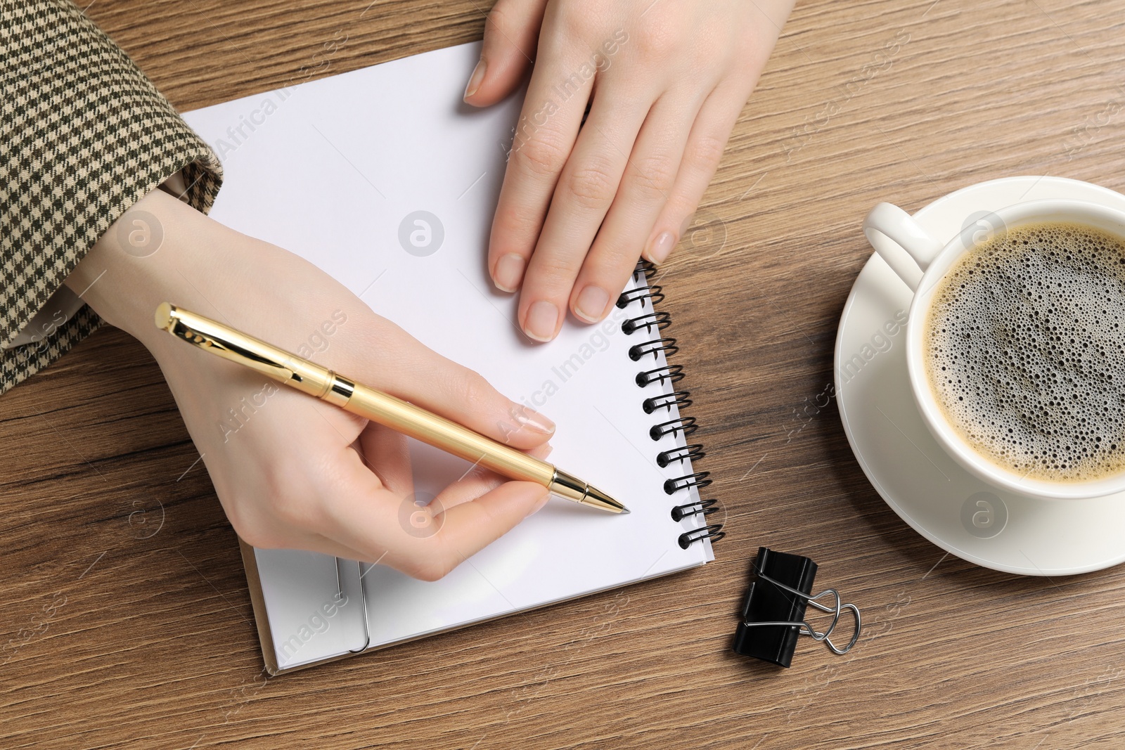 Photo of Woman writing in notebook at wooden table, top view