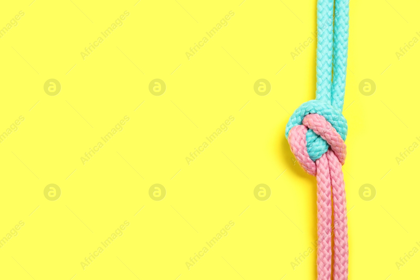 Photo of Top view of colorful ropes tied together on yellow background, space for text. Unity concept