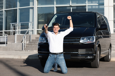 Excited man with key near car on city street. Buying new auto