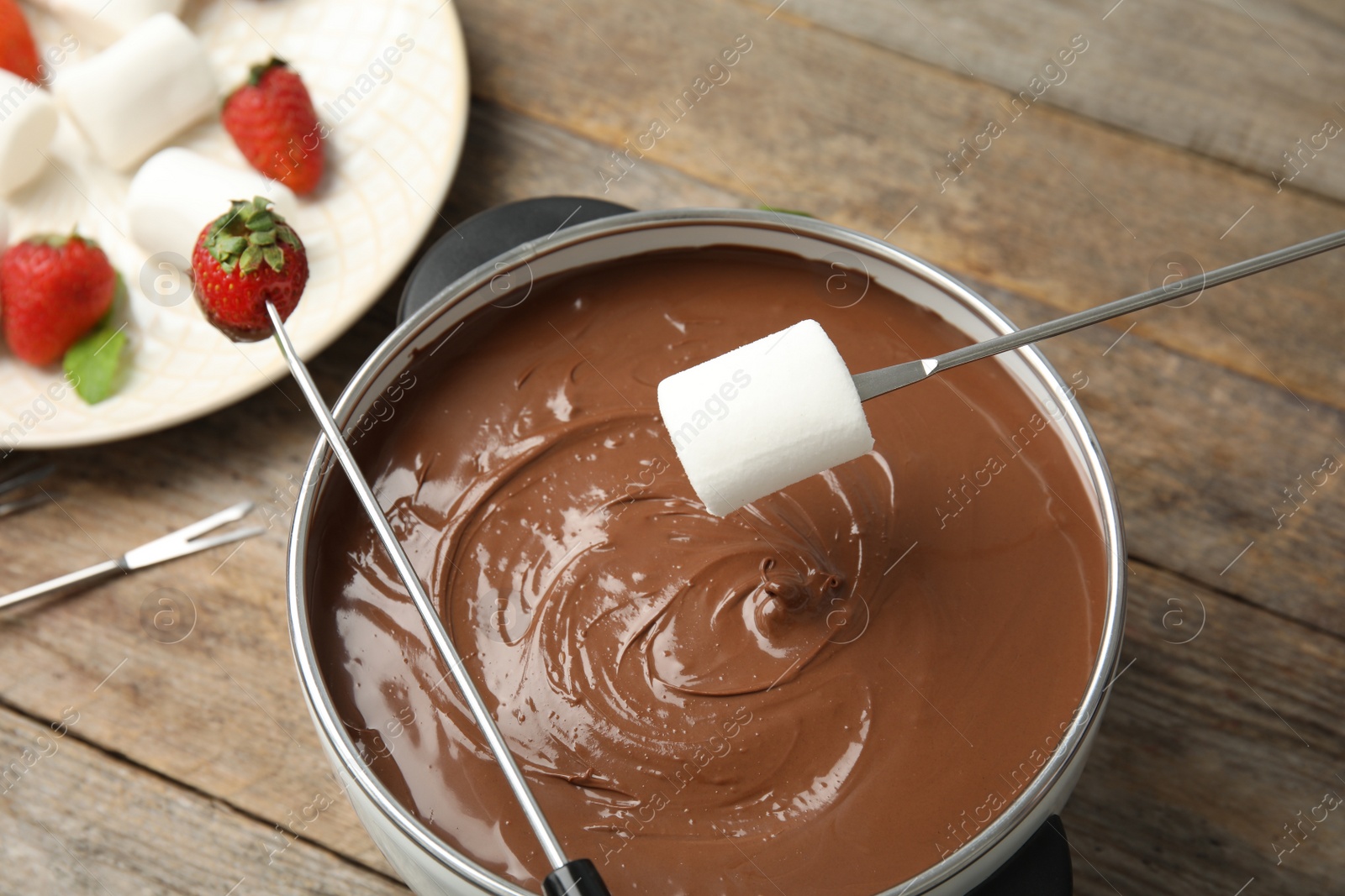 Photo of Dipping marshmallow into pot with tasty chocolate fondue on table