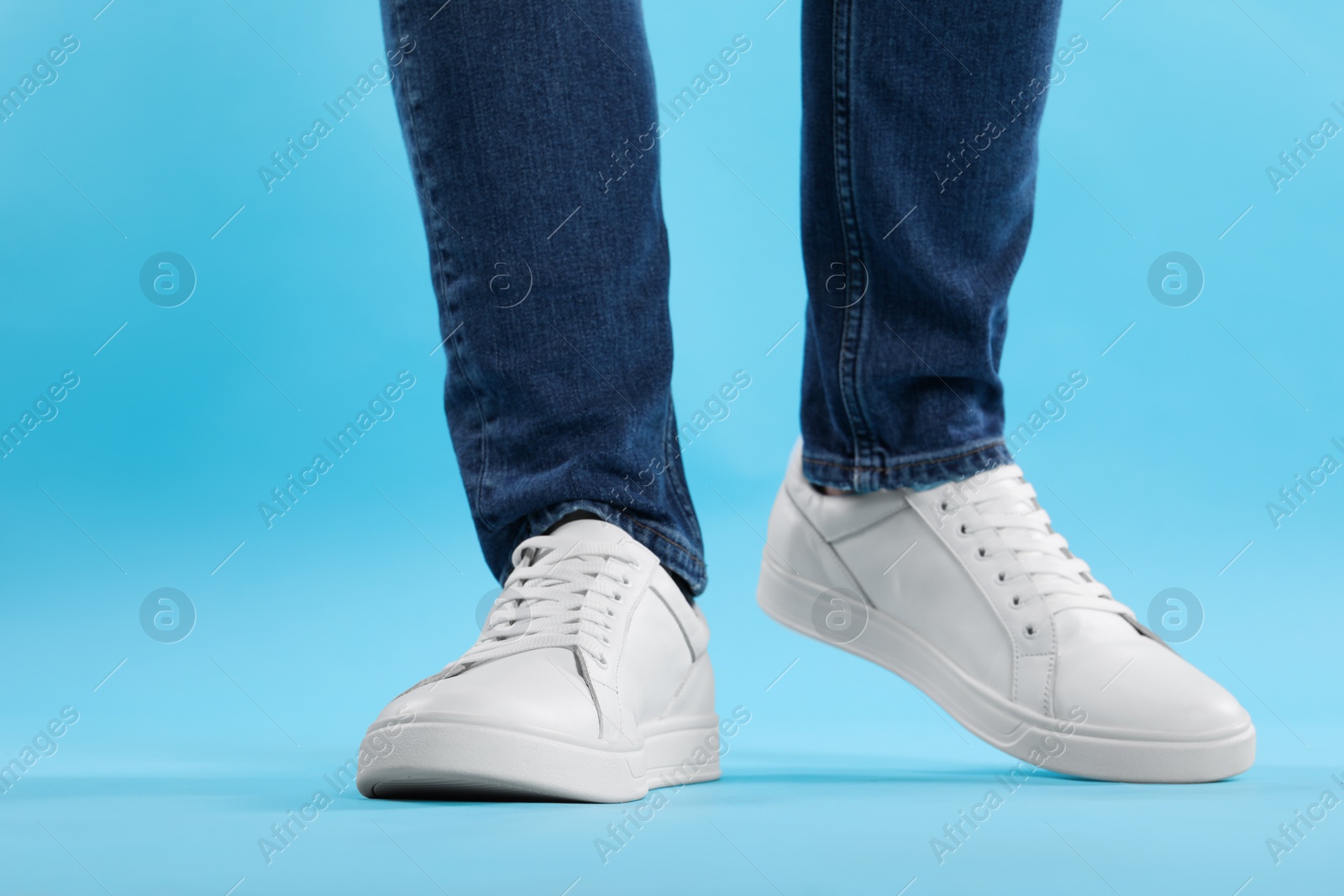 Photo of Man wearing stylish white sneakers on light blue background, closeup