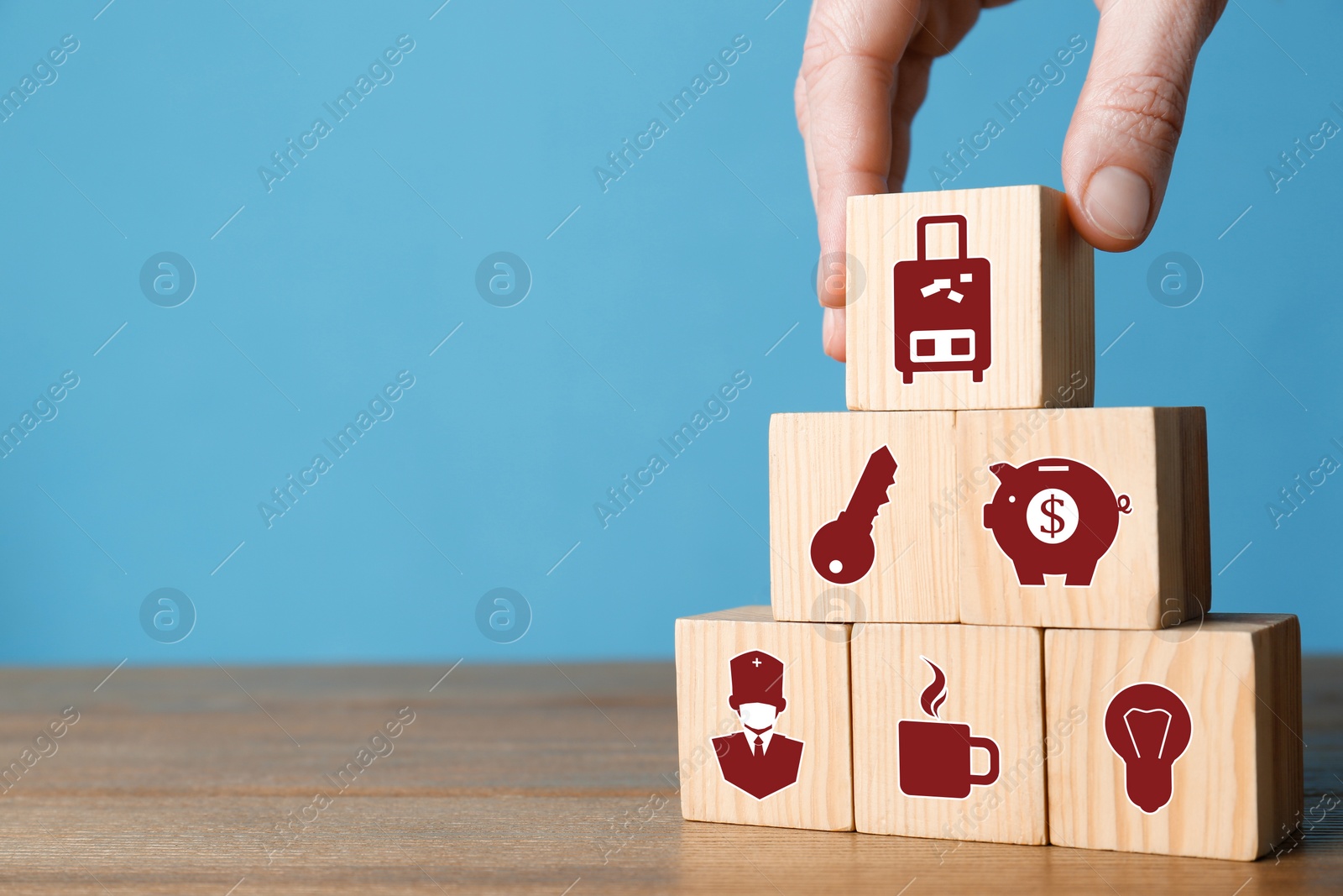 Image of Woman building pyramid of cubes with different icons on wooden table against light blue background, closeup. Insurance concept