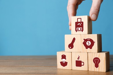 Image of Woman building pyramid of cubes with different icons on wooden table against light blue background, closeup. Insurance concept