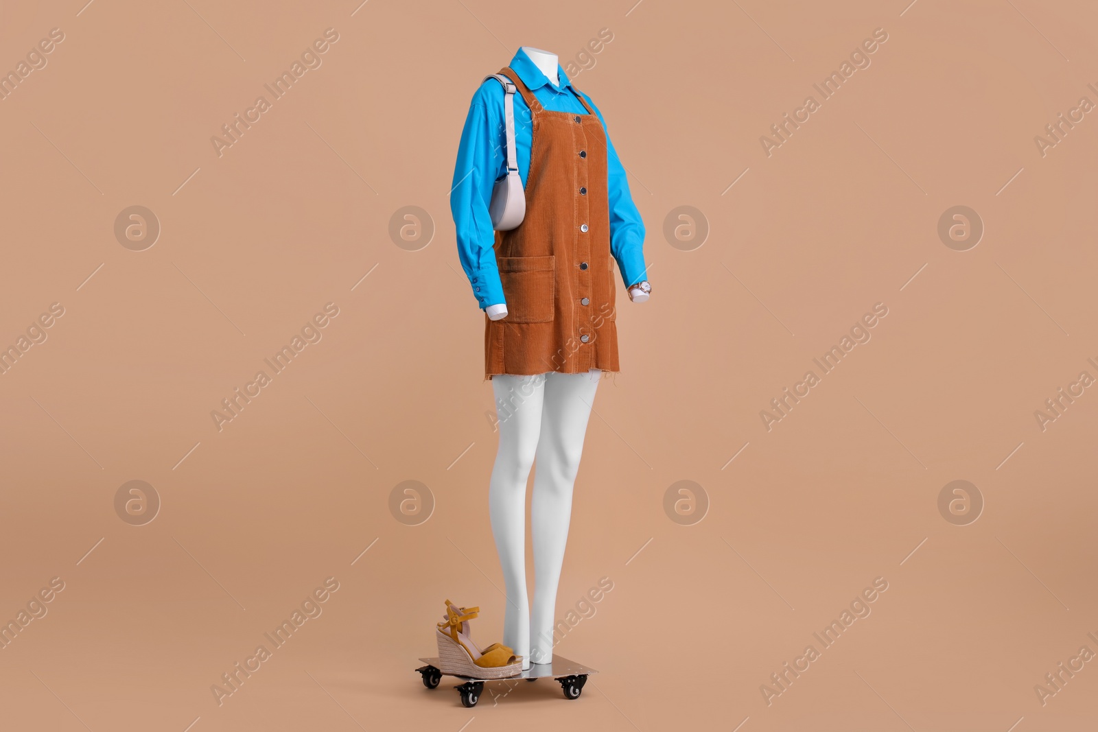 Photo of Female mannequin with accessories, sandals dressed in light blue shirt and orange jumper dress on beige background. Stylish outfit