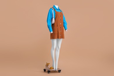 Photo of Female mannequin with accessories, sandals dressed in light blue shirt and orange jumper dress on beige background. Stylish outfit